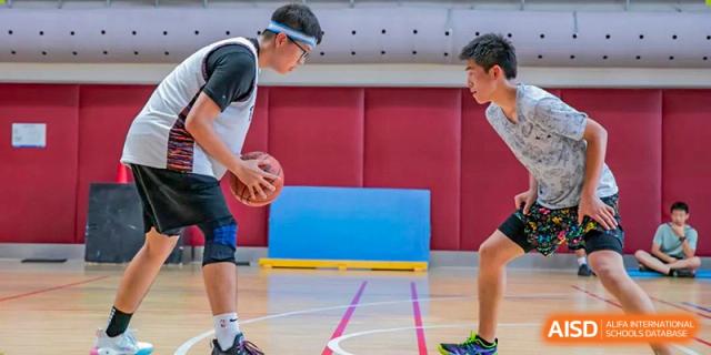 Two UWC Changshu China students in black and white uniforms playing basketball in a gym.