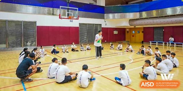 A UWC Changshu China coach instructing students sitting on a gym floor.