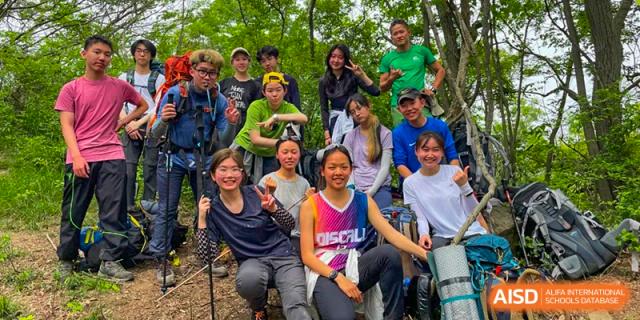 A group of UWC Changshu China students smiling together in a forest, wearing outdoor gear.
