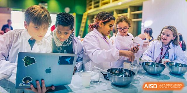 Western Academy of Beijing students in lab coats collaborate on a science experiment with a laptop.