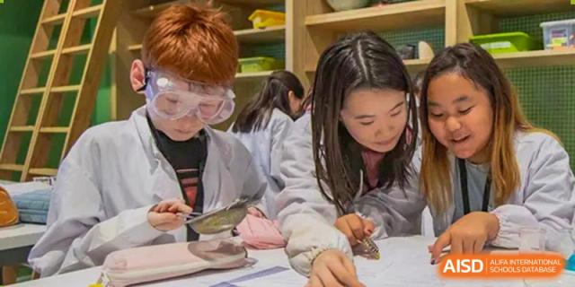 Western Academy of Beijing students, one wearing safety goggles, work together on a project at a table.