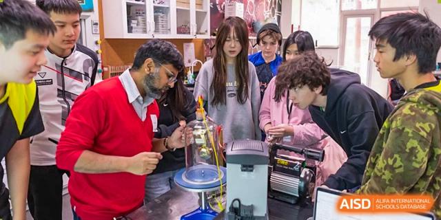 A Western Academy of Beijing teacher in a red sweater helps students with a project involving scientific equipment.