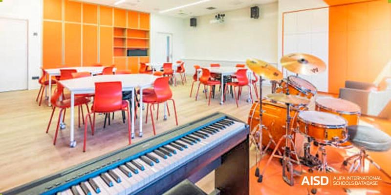 A music classroom at the Western Academy of Beijing with a piano, drum set, chairs, and tables.