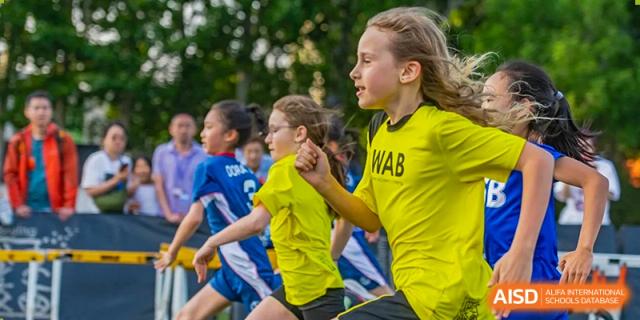Western Academy of Beijing female students running during a sports event on a grass field.
