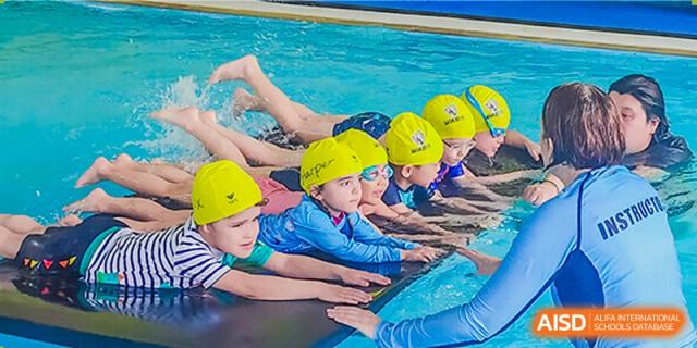 Western Academy of Beijing young swimmers in yellow caps and goggles learning with a teacher in an indoor pool.