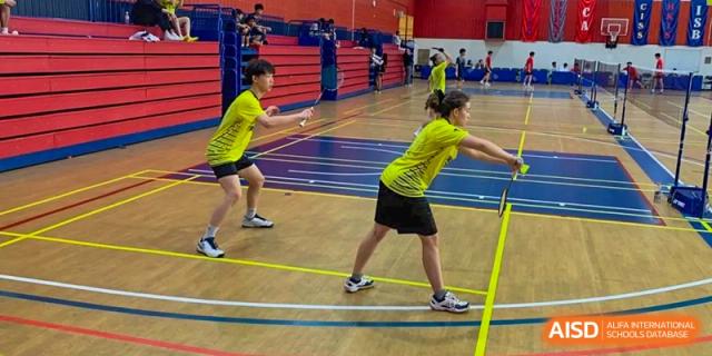 Two Western Academy of Beijing students playing badminton on an indoor court.