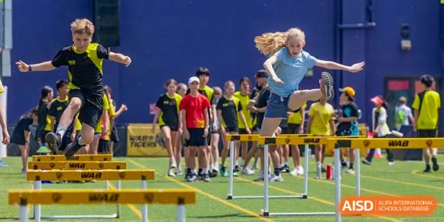 A Western Academy of Beijing student jumping over a hurdle during a track and field event.