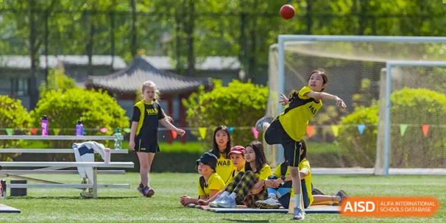 A Western Academy of Beijing student kicking a soccer ball while on the ground during a game.