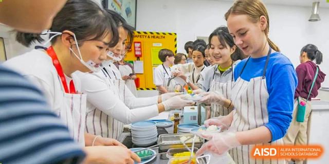 Western Academy of Beijing students in a kitchen or lab receive food while wearing aprons and gloves.