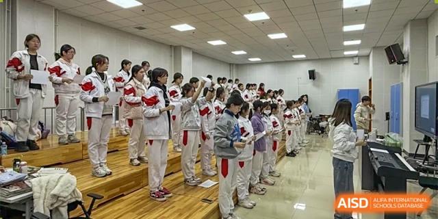 A line of students in white and red uniforms walks in a hallway, possibly during a school event or activity at the Xishan School of The High School Affiliated to Renmin University of China.