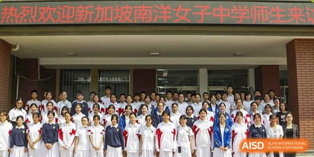 A large group of students in white and red uniforms is posed for a photo in front of a school building at the Xishan School of The High School Affiliated to Renmin University of China.