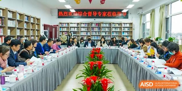 A meeting or conference is taking place in a room with a long table, with several people seated around it and bookshelves in the background at the Xishan School of The High School Affiliated to Renmin University of China.
