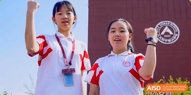 Two students, wearing white shirts and lanyards, are seen smiling at a camera with a crowd behind them at the Xishan School of The High School Affiliated to Renmin University of China.