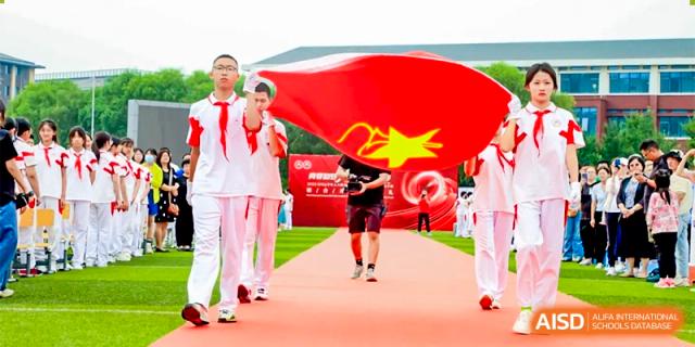 Xishan School of The High School Affiliated to Renmin University of China students carrying a large Chinese flag during an outdoor event.