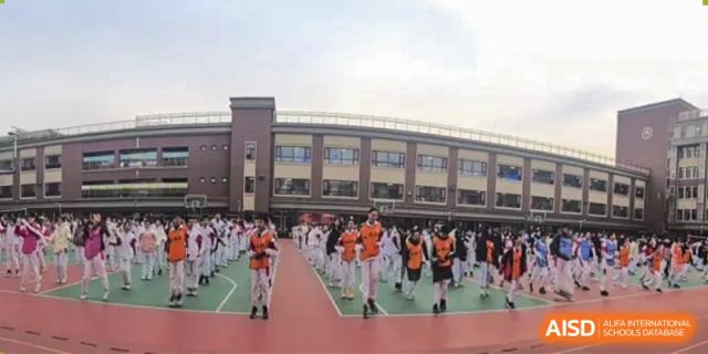 A group of students in orange and black uniforms perform a synchronized routine on an outdoor court at the Xishan School of The High School Affiliated to Renmin University of China.
