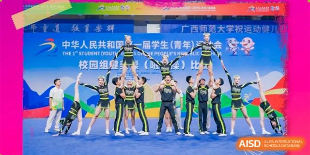 A cheerleading team in black and yellow uniforms with pom-poms performs a stunt, with one student being held aloft by others at the Xishan School of The High School Affiliated to Renmin University of China.