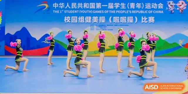 A group of female cheerleaders in black and yellow outfits with pom-poms performs a synchronized routine on a stage at the Xishan School of The High School Affiliated to Renmin University of China.