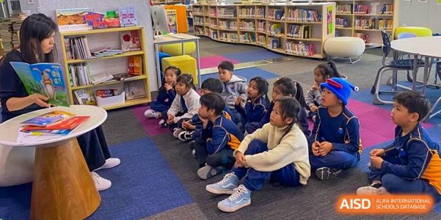 Students at Yew Wah International Education School Of Beijing Yizhuang Campus are seated on the floor in a classroom.