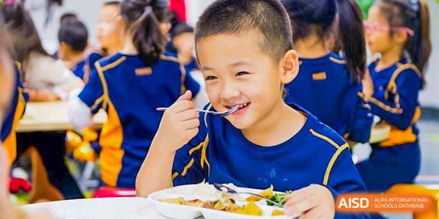 A child at Yew Wah International Education School Of Beijing Yizhuang Campus smiles while eating.
