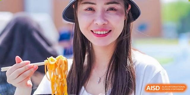 A woman at Yew Wah International Education School Of Beijing Yizhuang Campus smiles while holding noodles.