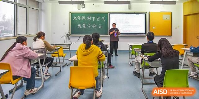 A classroom scene with a teacher lecturing near a blackboard with Chinese characters and students seated at Yitian Hudson School.