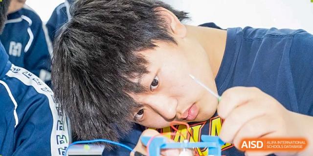 An extreme close-up of a male student with his head down, deeply concentrating or resting on his arm in a classroom setting at Yitian Hudson School.