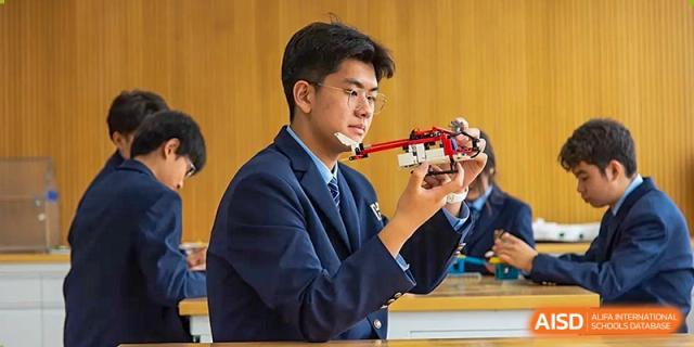 A male teacher or older student in a suit demonstrating how to assemble or work with a complex robot or science model at Yitian Hudson School.