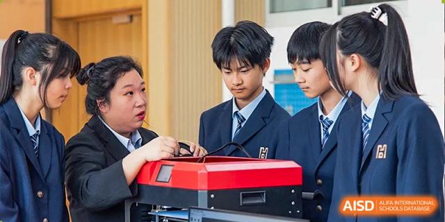Two male students in school uniforms working together on a red and black 3D printer or complex science model at Yitian Hudson School.
