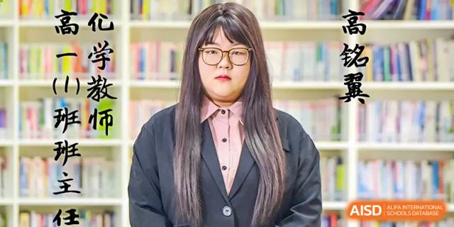A female student in a formal black suit and glasses posing for a portrait in a library or learning center at Yitian Hudson School.