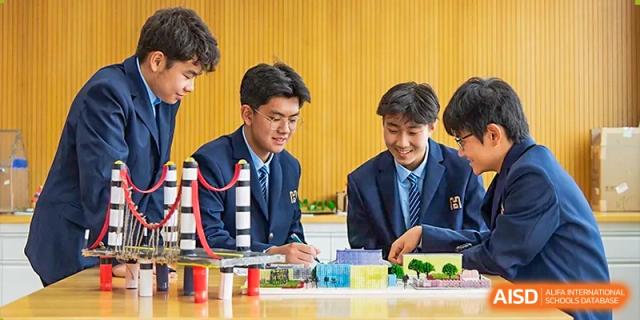 Two male students in uniform building structures with colorful plastic blocks during a design or engineering class at Yitian Hudson School.