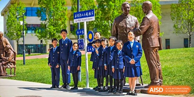 A group of younger students in dark blue uniforms standing with an adult, possibly a teacher or community leader, in an outdoor setting at Yitian Hudson School.