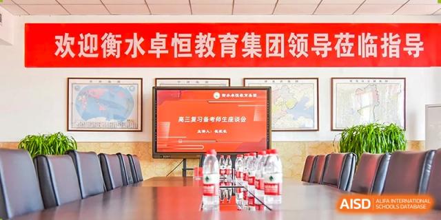 A close-up of a table in a meeting room showing a screen display with Chinese text and a row of bottled water, indicating a school leadership meeting or event at Yitian Hudson School.