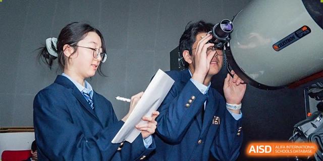A person in a dark suit reviewing a document or test paper during a meeting or class session at Yitian Hudson School.