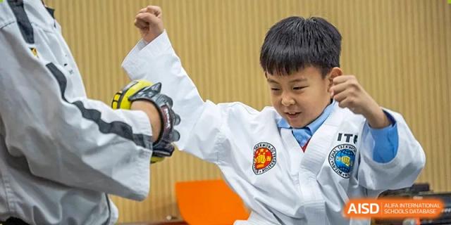 A young boy in a white martial arts uniform with a school badge practicing a strike or block at Yitian Hudson School.