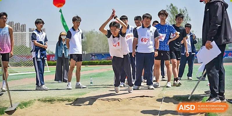 Students cheering and clapping in a line at an outdoor sports event, possibly after a long jump, at Yitian Hudson School.