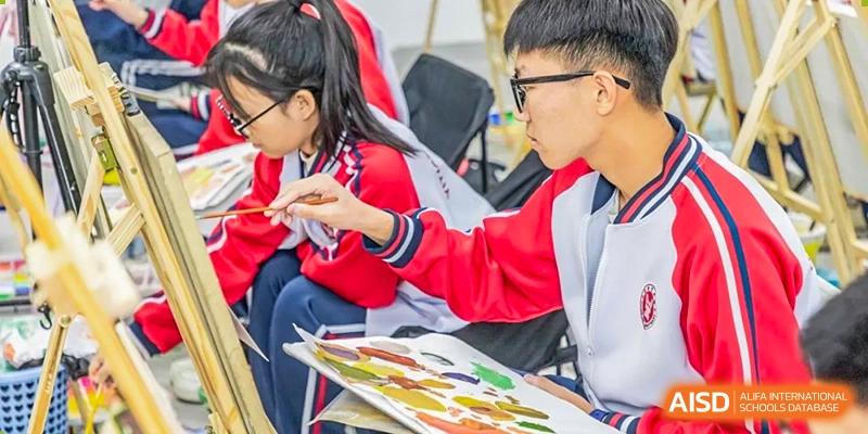 Two students in red and white uniforms focusing on a colorful painting project during an art class at Yitian Hudson School.