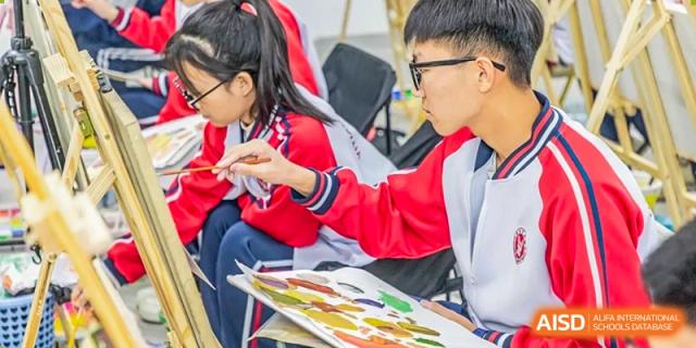 Two students in red and white uniforms focusing on a colorful painting project during an art class at Yitian Hudson School.