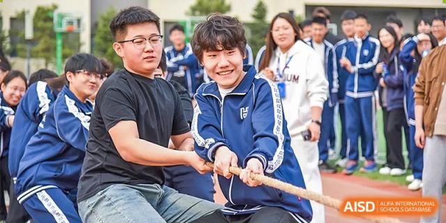 A smiling student pulling on a rope during a tug-of-war game with other students and adults at an outdoor event at Yitian Hudson School.