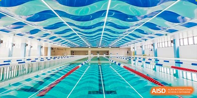 A bright, indoor swimming pool with clear water, lane lines, and a unique blue and white wave-patterned ceiling at Yitian Hudson School.