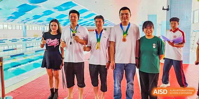 Three men, possibly teachers or coaches, standing and smiling while wearing gold medals after a sports event at Yitian Hudson School.