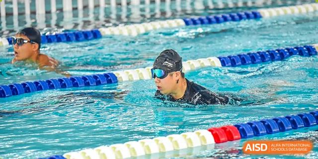 A student or athlete swimming with goggles and a cap in a blue, indoor swimming pool at Yitian Hudson School.
