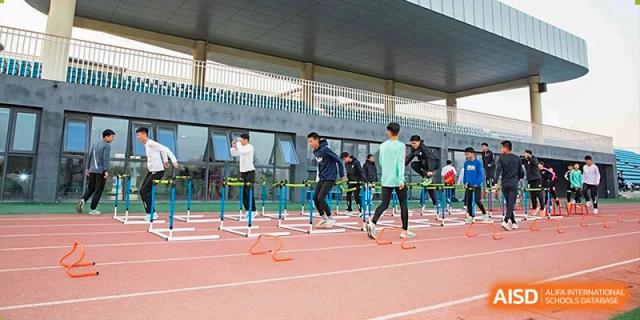 Students and a coach participating in an outdoor agility drill using low hurdles on a red track at Yitian Hudson School.