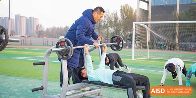 A student lying on a bench while an instructor assists them in a weightlifting or strength training session outdoors at Yitian Hudson School.