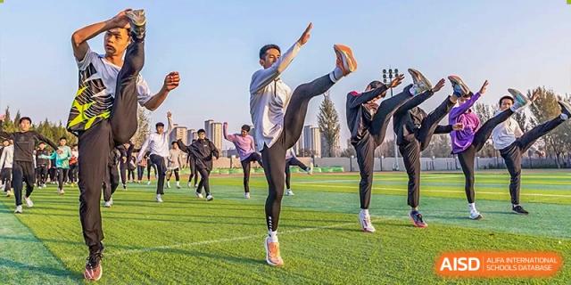 A group of students participating in outdoor martial arts or fitness training, with one student performing a high kick on a sports field at Yitian Hudson School.
