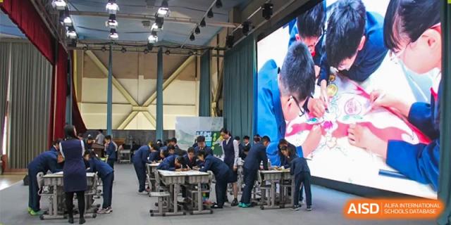 A group of students at ZHAA group of students at ZHANGQIU BILINGUAL INTERNATIONAL SCHOOL works collaboratively in groups around small tables in a large indoor space.