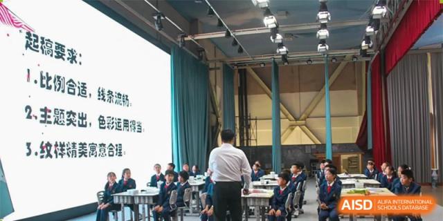 A teacher at ZHANGQIU BILINGUAL INTERNATIONAL SCHOOL instructs a large group of students in an assembly or lecture setting.