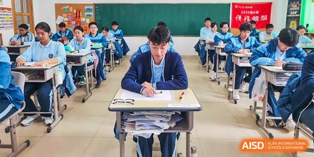 A male student at ZHANGQIU BILINGUAL INTERNATIONAL SCHOOL  focuses intently while taking a test or writing an assignment at his desk.