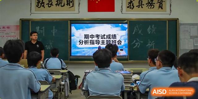 Students at ZHANGQIU BILINGUAL INTERNATIONAL SCHOOL face a screen displaying a message in Chinese about exam results and guidance in a classroom.