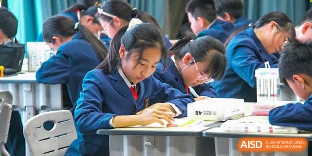 A female student at ZHANGQIU BILINGUAL INTERNATIONAL SCHOOL in a navy blazer focuses on her work during a test or class activity.