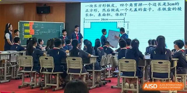 Students at ZHANGQIU BILINGUAL INTERNATIONAL SCHOOL sit at desks facing a presentation screen with Chinese text in a classroom.